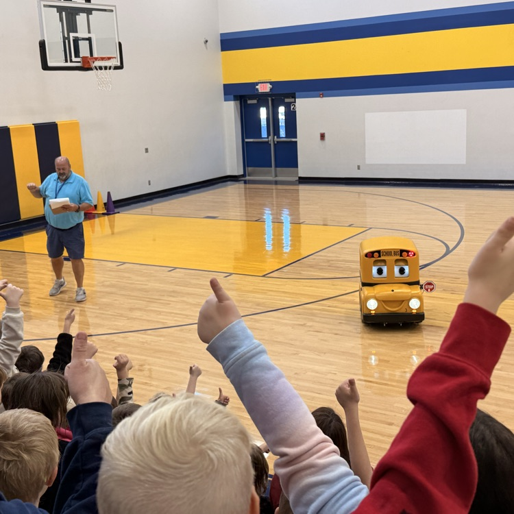 Students in gym giving electronic Buster the Bus a thumbs up for bus safety. 