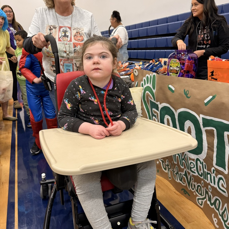 Little girl with brown hair in a rolling chair trick or treating in gym 