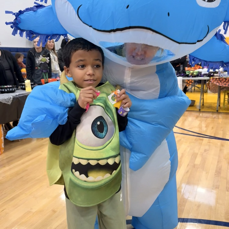 Little big in a Monster’s Inc costume hugging an inflatable blue dinosaur 