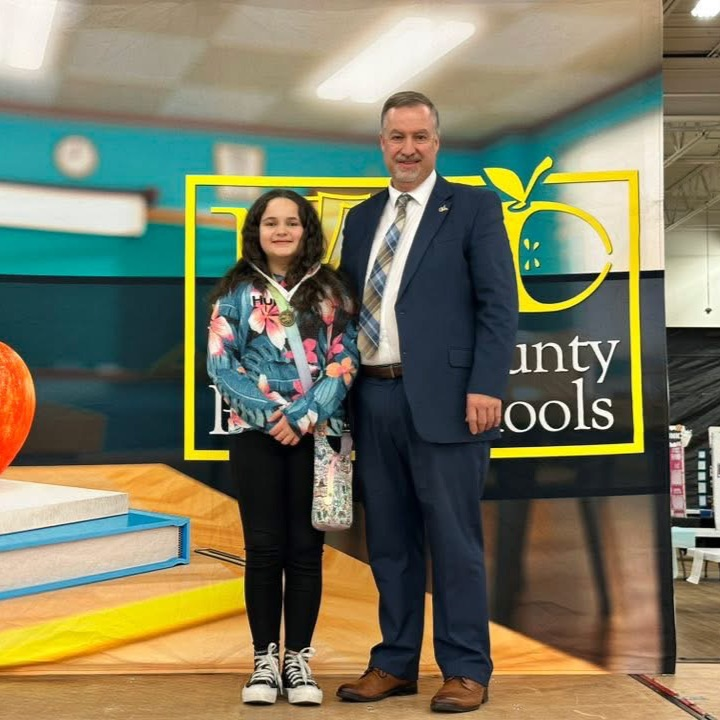 Brown hair girl standing with man taking a picture with her new 1st place science fair medal. 