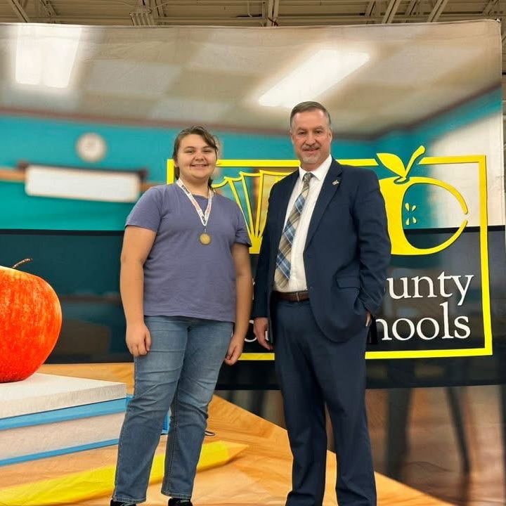 Taller blonde hair girl standing with man taking a picture with her new 1st place science fair medal. 