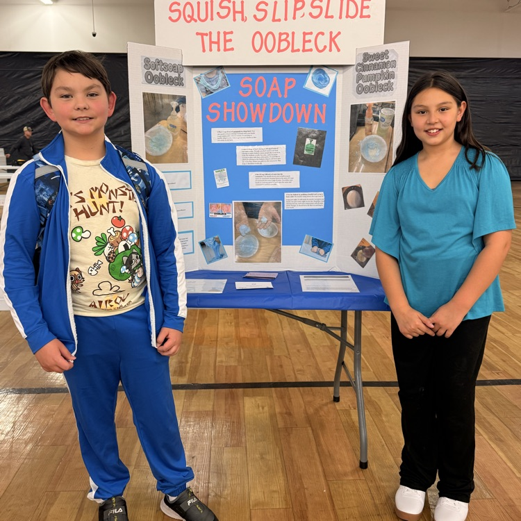 A boy and a girl standing in front of their Oobleck science fair project  
