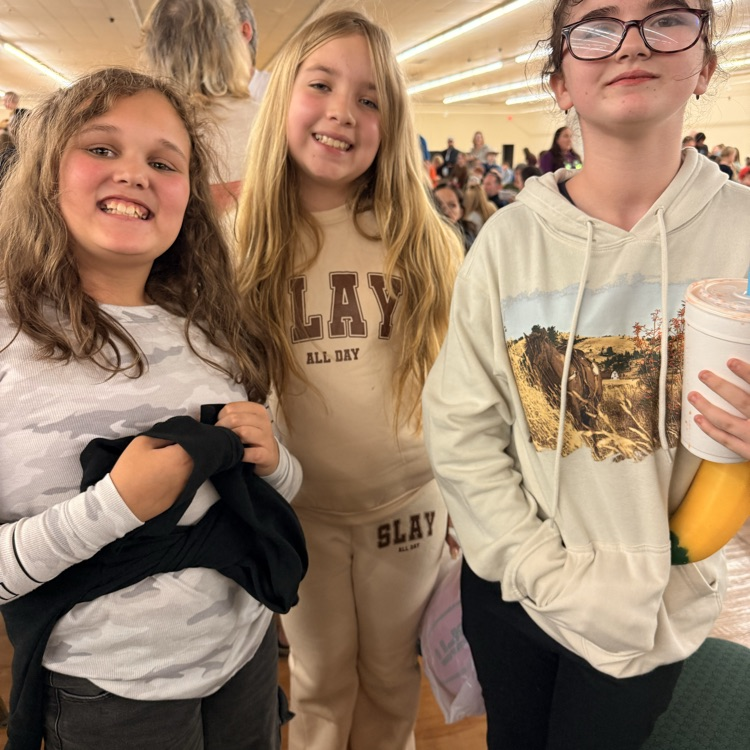 3 elementary girls posing for a picture. One girl has brown curly hair, middle child hair longer blonde hair and right girl had brown hair pulled back in a pony tail with glasses on her face  
