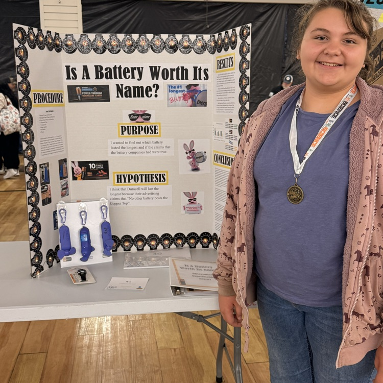 Taller , 1st place blonde girl standing in front of her science fair project. The project is titled “Is a Battery Worth its Name?”