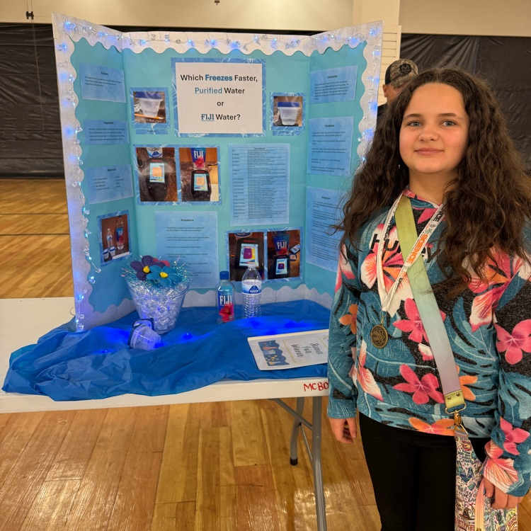 Girl with long curly hair, 1st place winner is standing in front of her water freezing project.