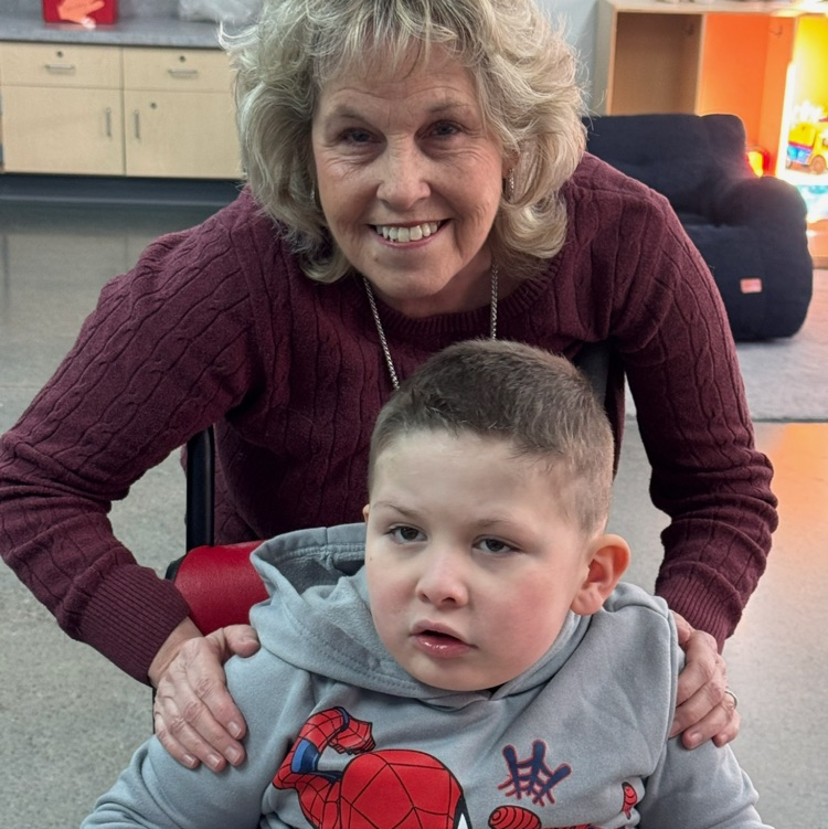 Picture is of school counselor Mrs. Belcher in a maroon shirt standing behind a sitting child in a Spider-Man sweatshirt  