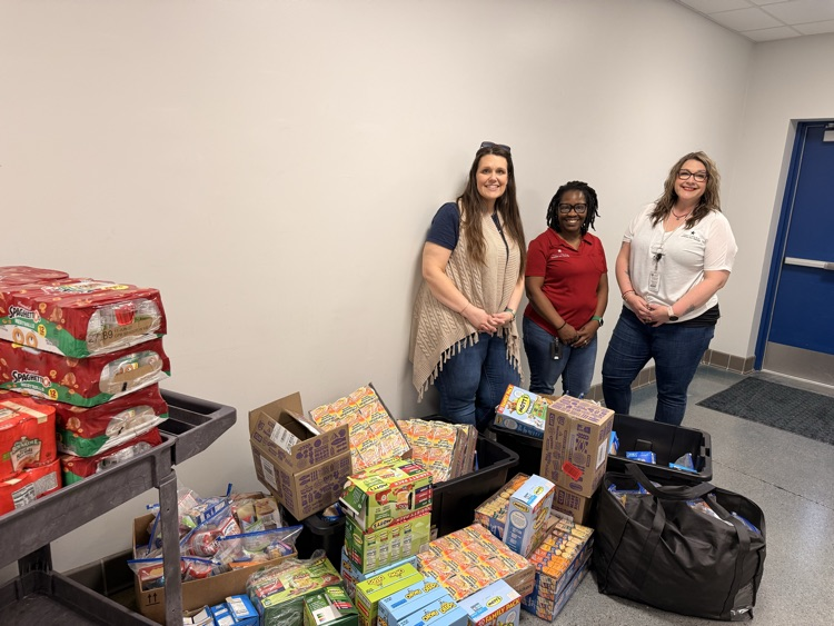 Three women standing behind a huge donation of food items  