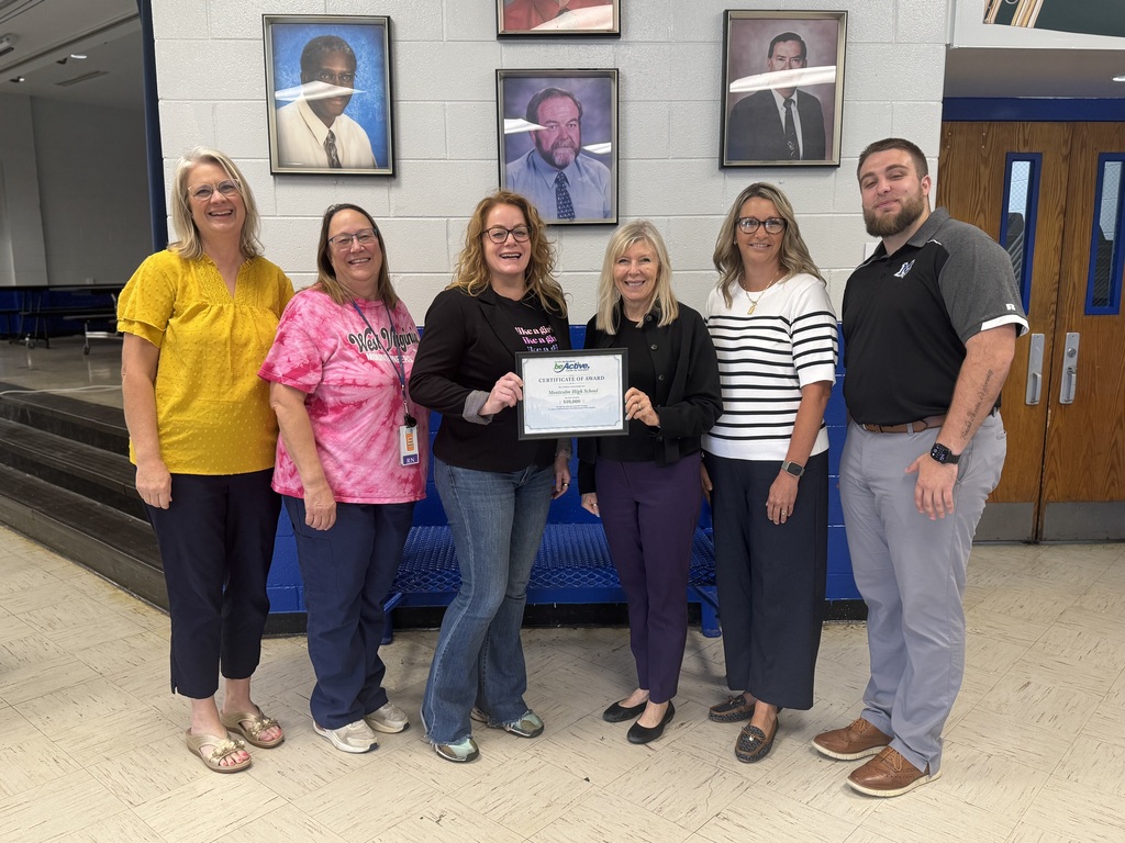 Six adults stand next to each other in a room. One holds an award certificate.