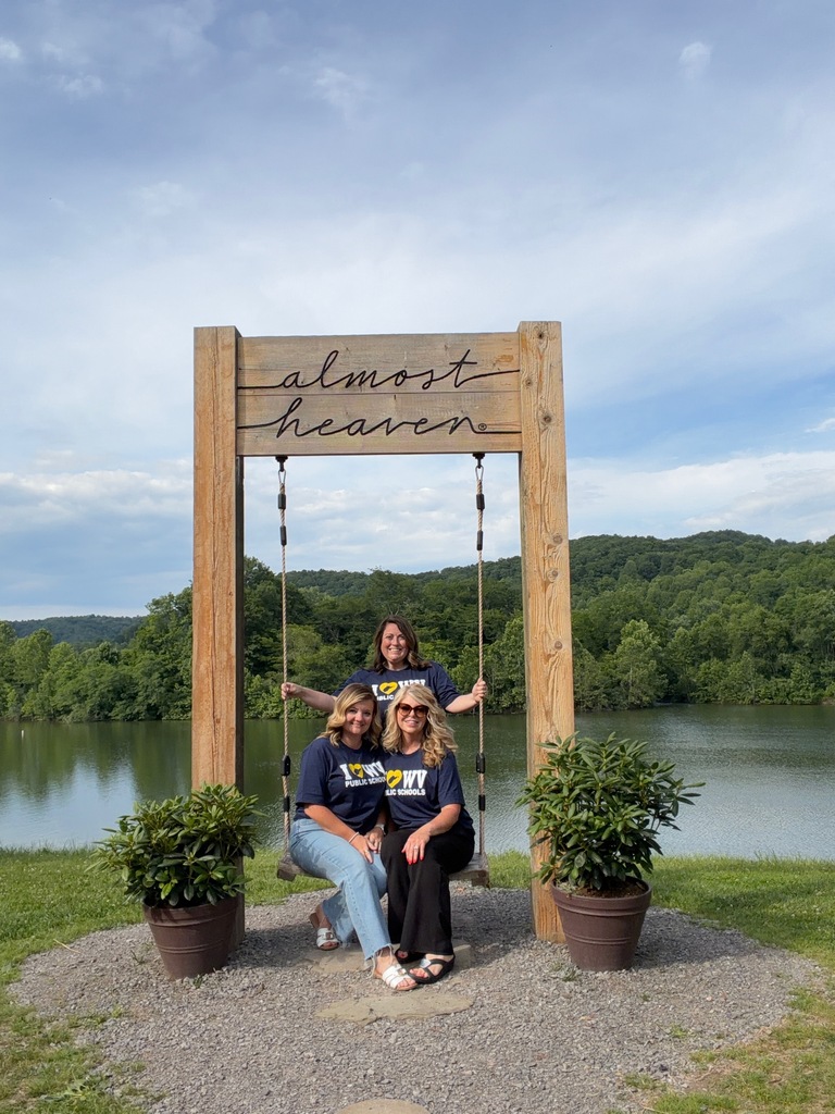 Three women in blue shirts posing in front of a body of water