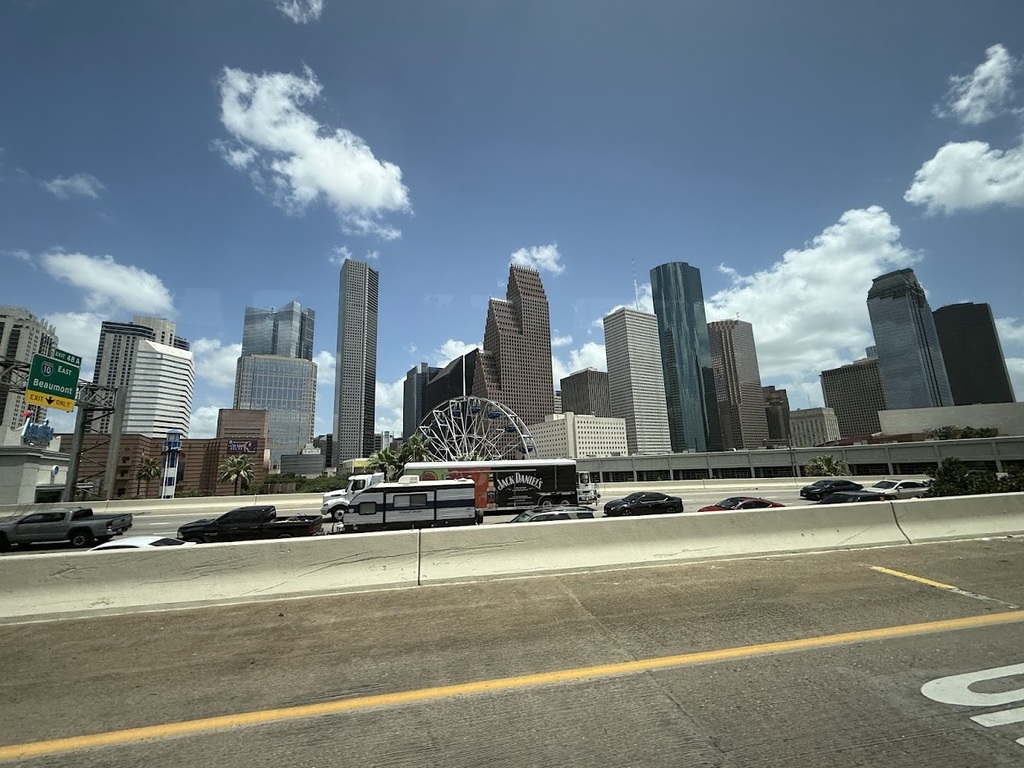 Urban landscape with a clear blue sky, high-rise buildings, and a busy road with several vehicles.