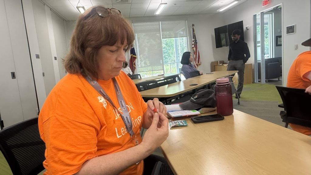 A woman in an orange shirt sitting at a desk, working on a project with a notebook.