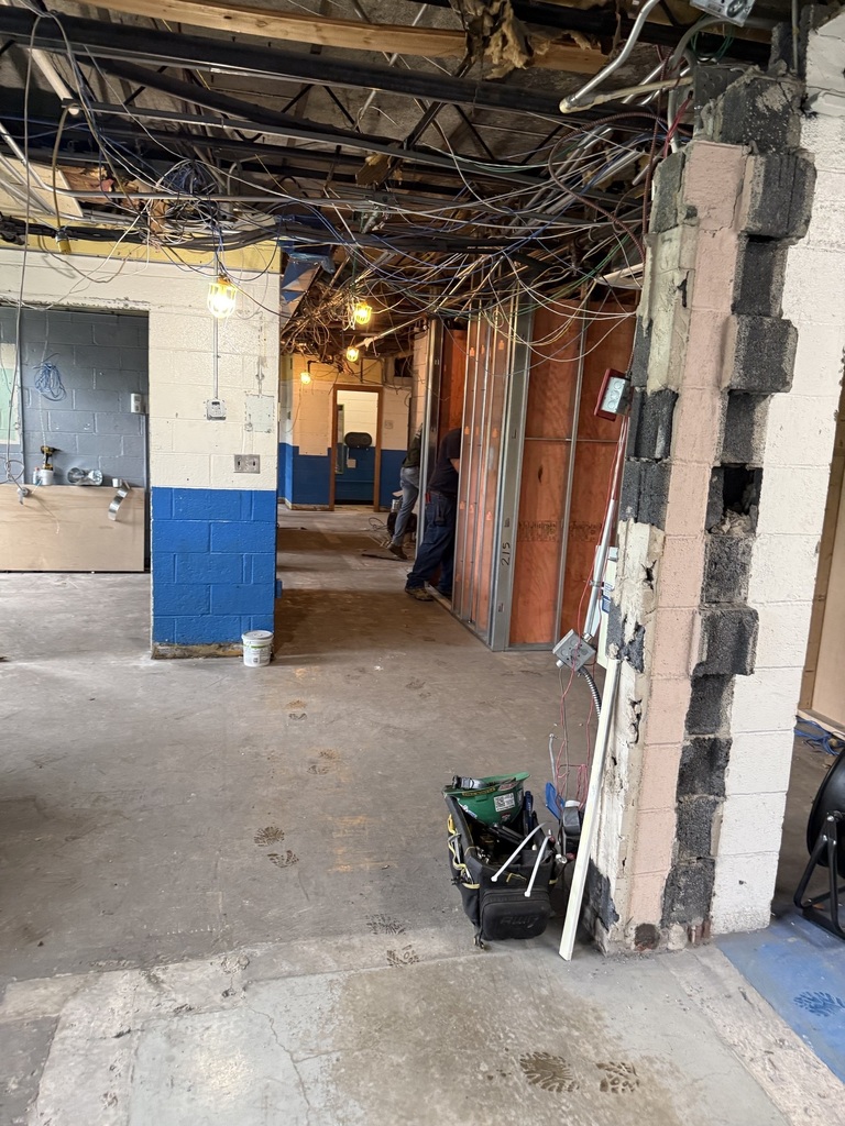 A construction site with exposed beams, blue and white walls, and various tools and materials on the floor.
