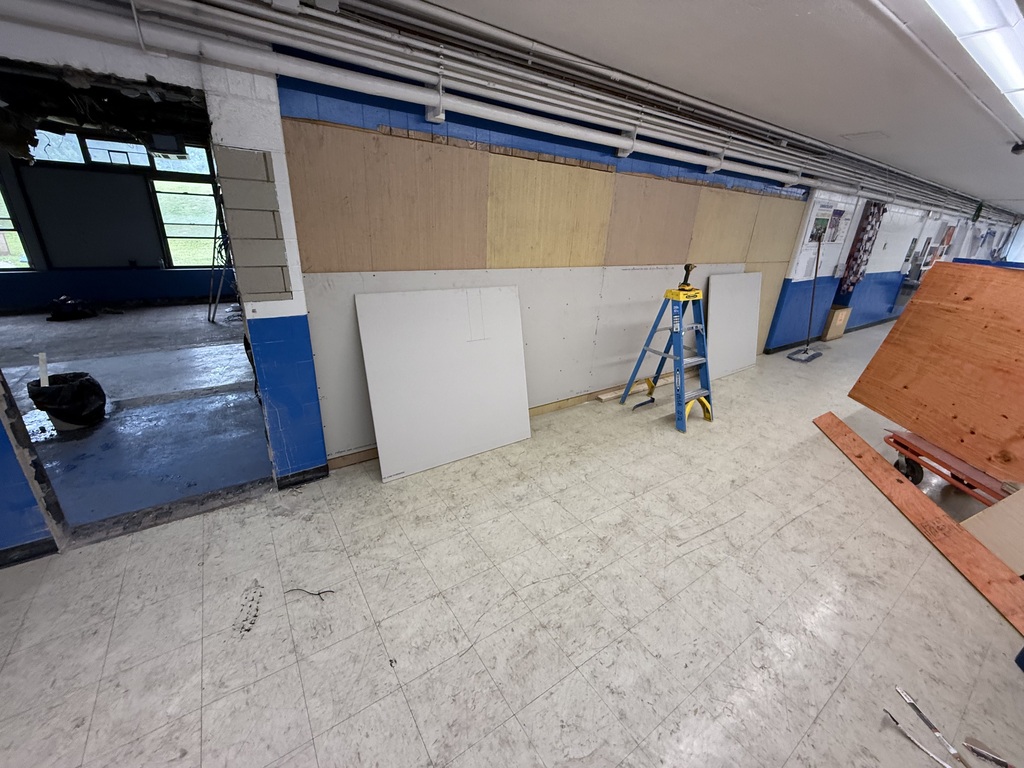 Interior of a room with an open door, tiled floor, and unfinished walls. A blue ladder, white boards, and wooden planks are in the room.