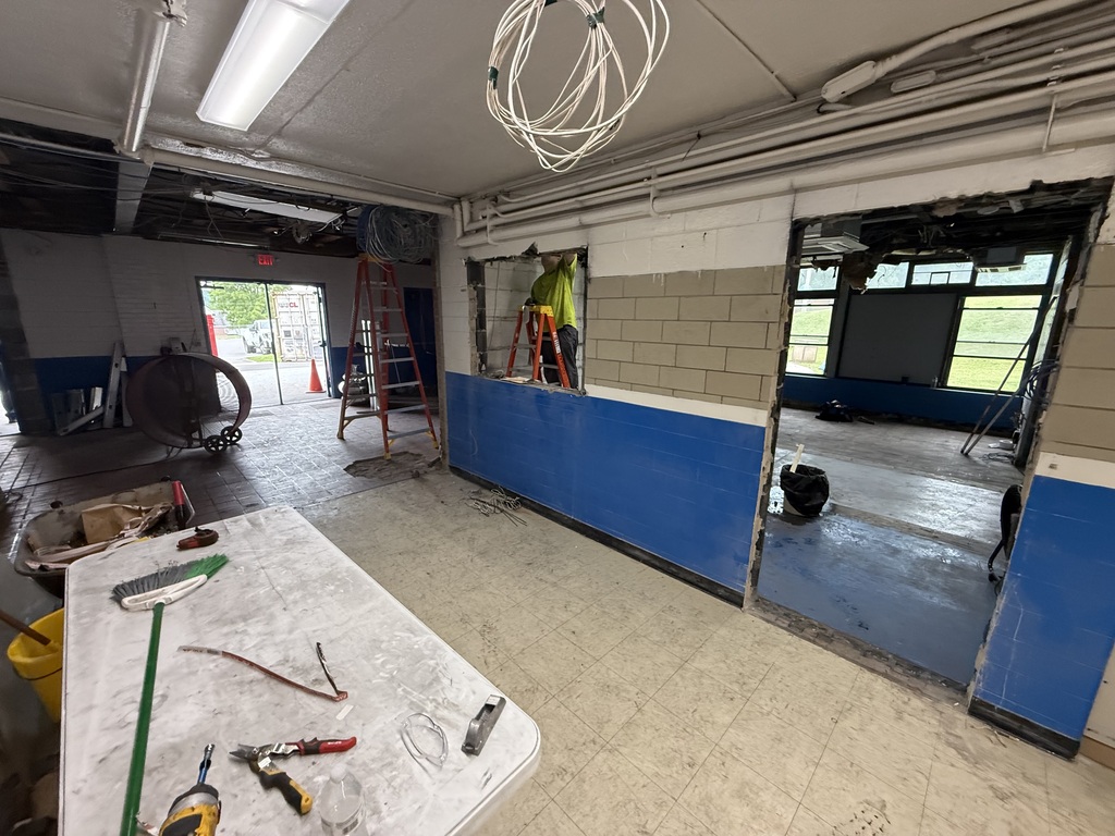 Interior of a room under construction with a table, tools, ladder, and an open doorway. Blue and white walls.