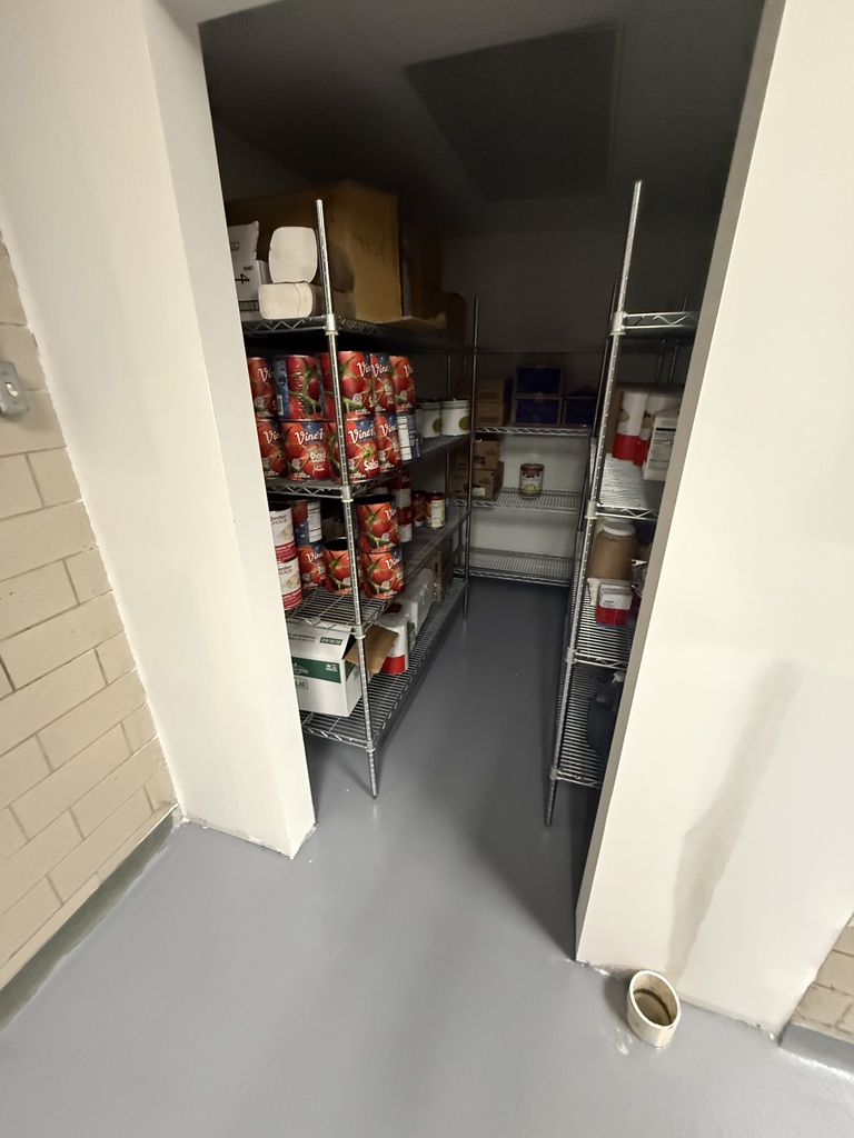 Interior of a storage room with open shelves, canned goods, boxes, and a tiled floor.