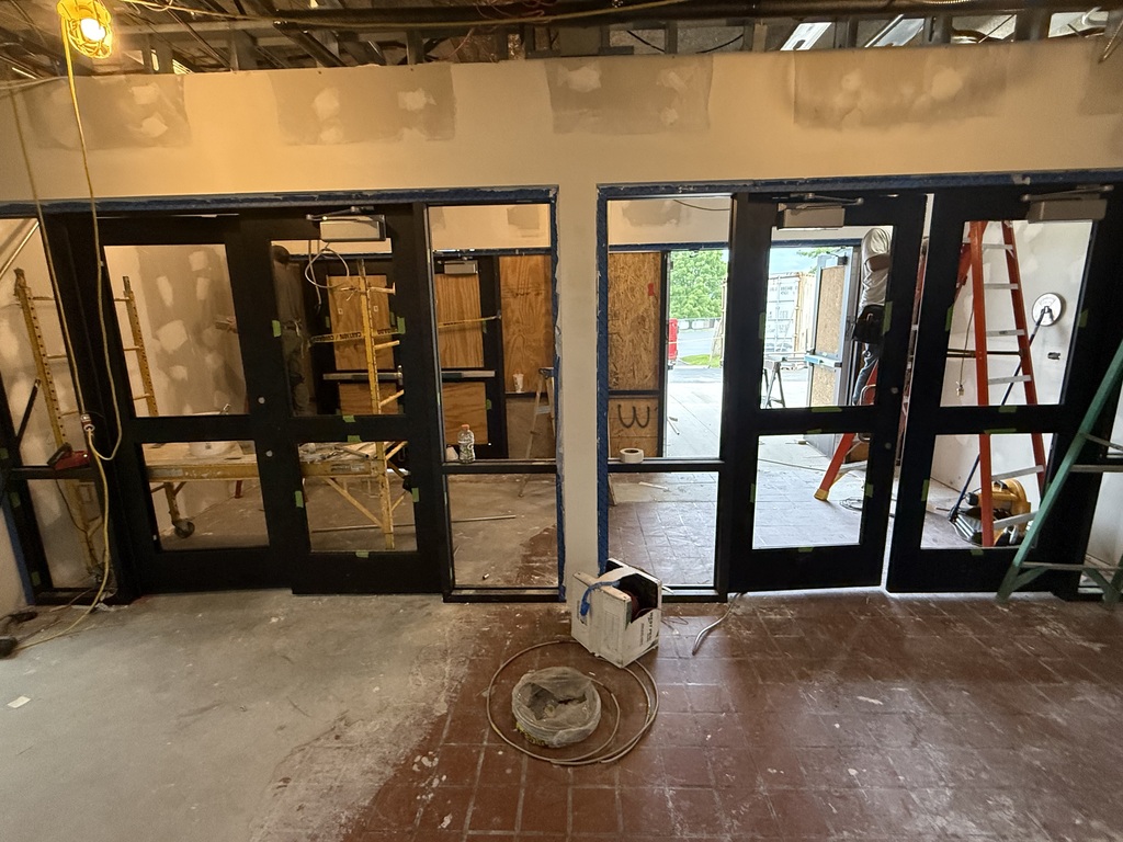 An empty room with black-framed doors and windows. The floor is unfinished, with a white object in the center. Tools are visible in the background.