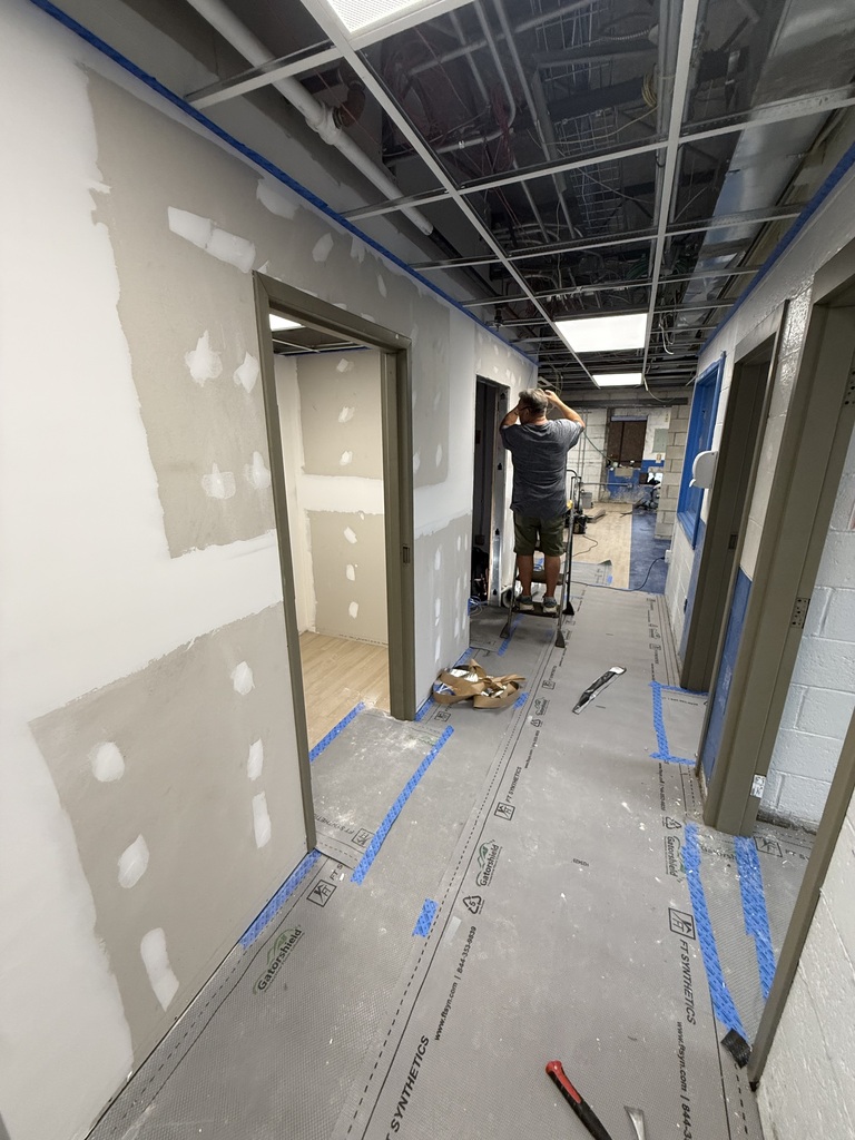A hallway under construction with gray walls and white trim. A person works with tools and materials.