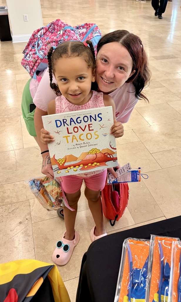 A child with her parent. The child is holding a book titled Dragons Love Tacos