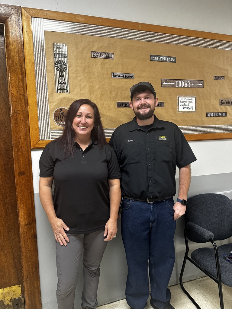 A man and a woman stand next to each other in a room with a large poster in the background.