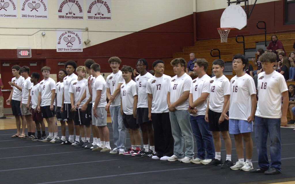 Row of young men in white shirts and sneakers standing on a track, facing the audience.