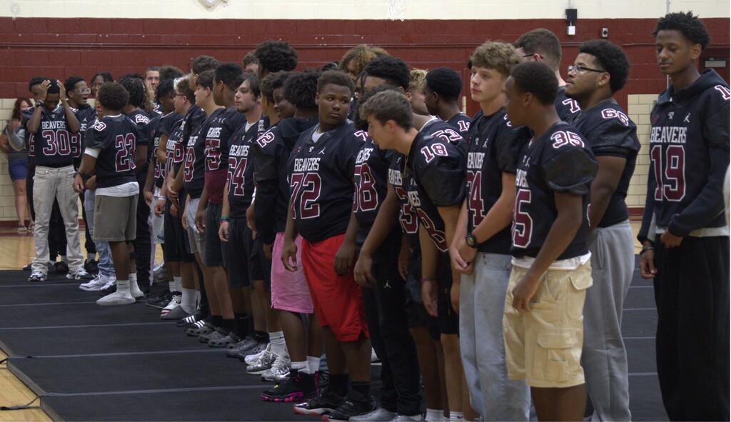 A row of football players in black jerseys with numbers on the back, standing in a line.