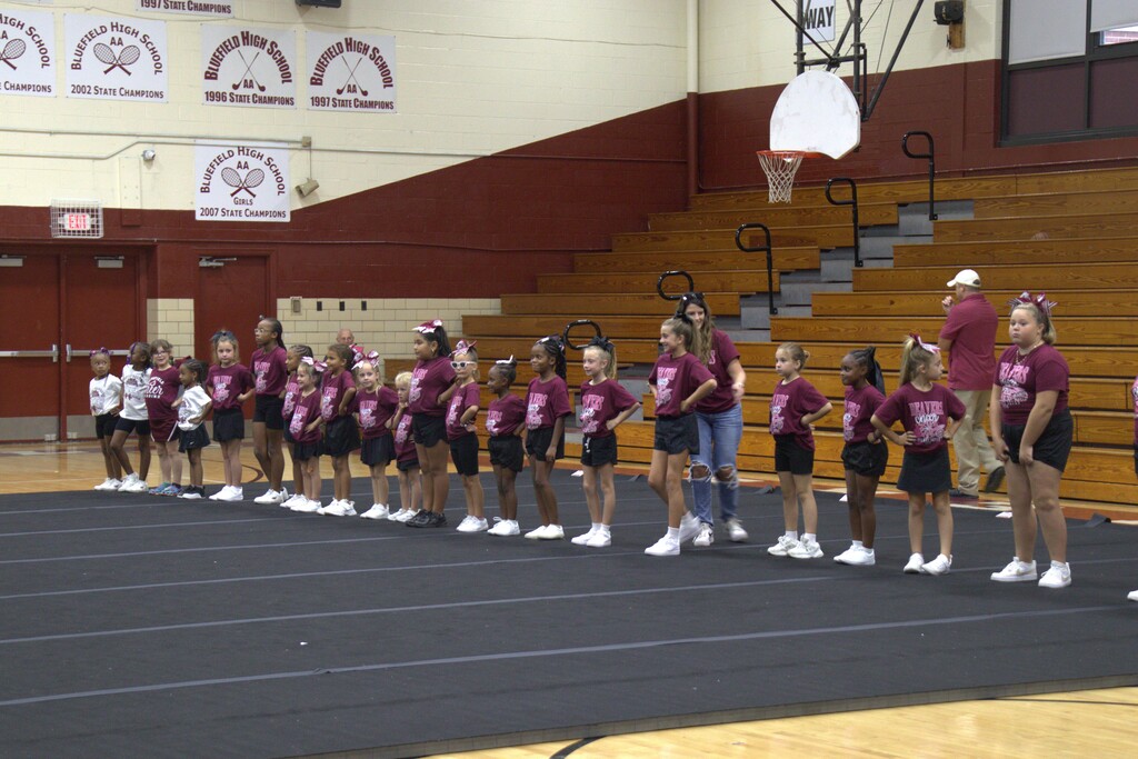A group of children in matching shirts and shorts on a gym floor, with adults standing in front.