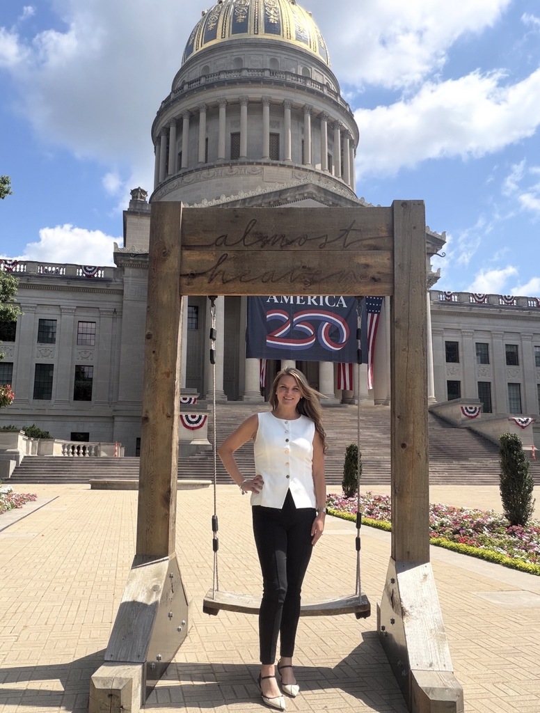 A woman stands in front of a wooden swing in front of a large building with a dome.
