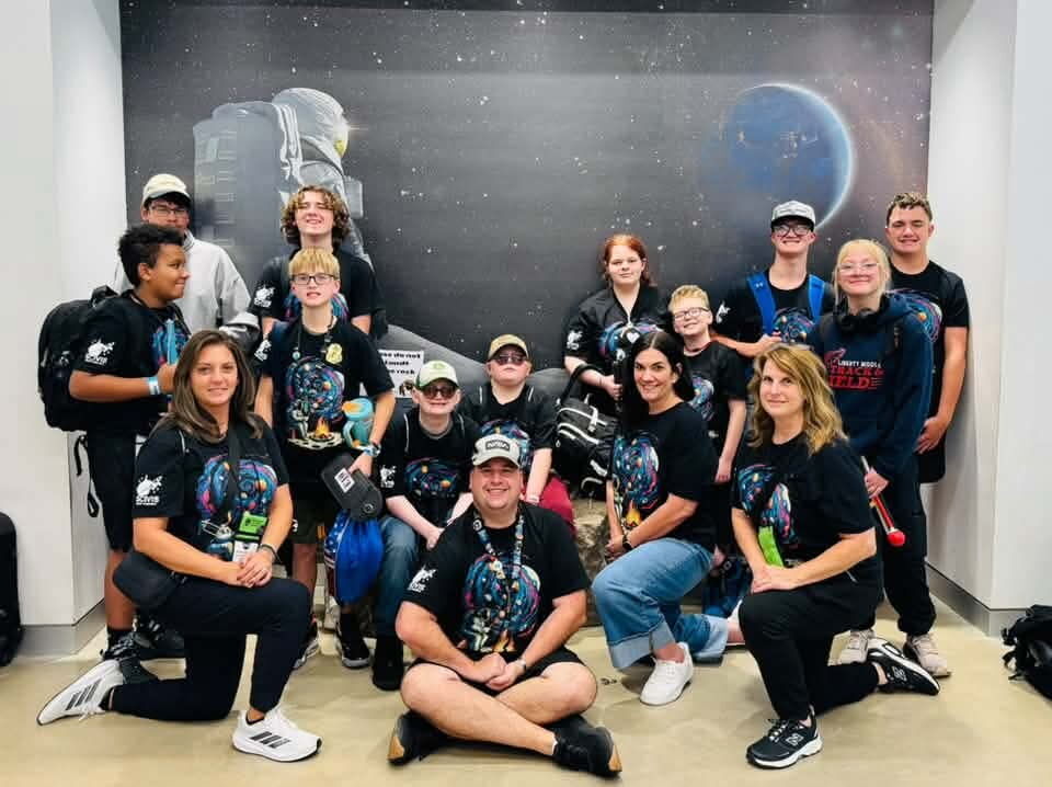 People pose for a photo in front of a wall featuring a mural of a space shuttle.