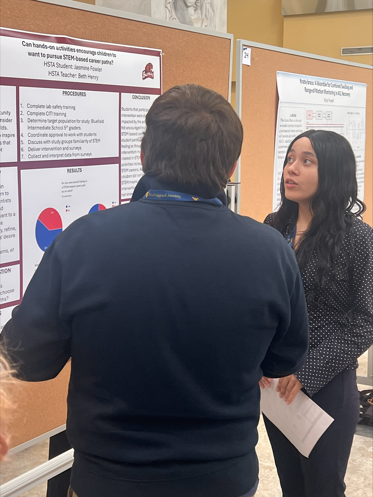 Two people in a hall with posters on the wall. One person looks at a poster while the other person holds a paper.