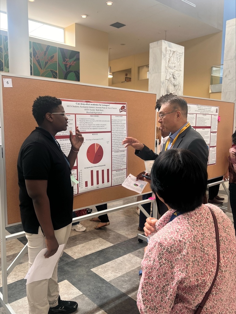 Two men and two women gather around a poster, discussing a chart on it in a conference room.