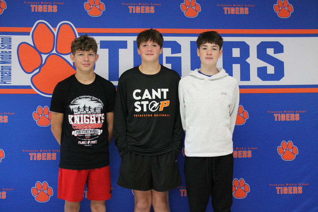 Three boys in athletic wear stand in front of a wall with "Tigers" text and paw prints.