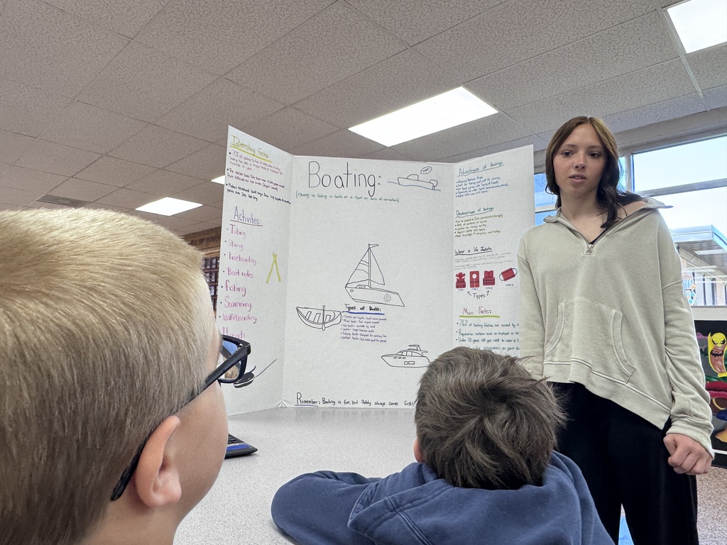Student beside tri-fold display As younger students watch presentation