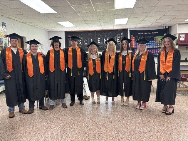 9 graduates in black gowns and caps with orange stoles