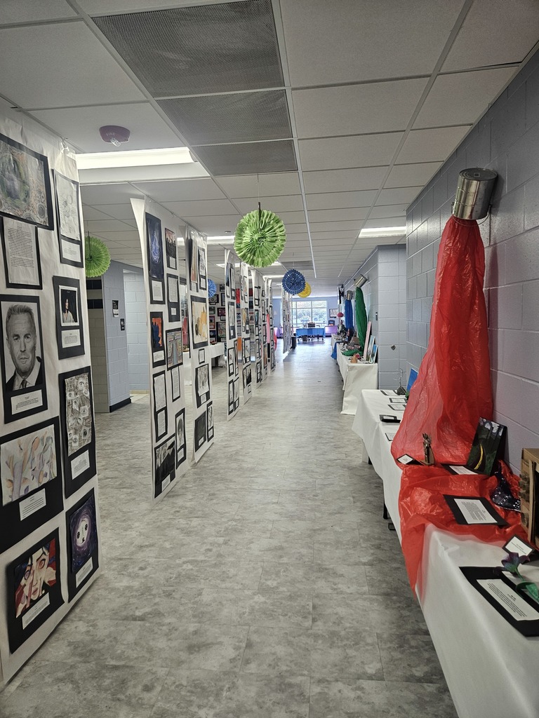 High school art projects displayed on white paper panels hanging from the ceiling. 