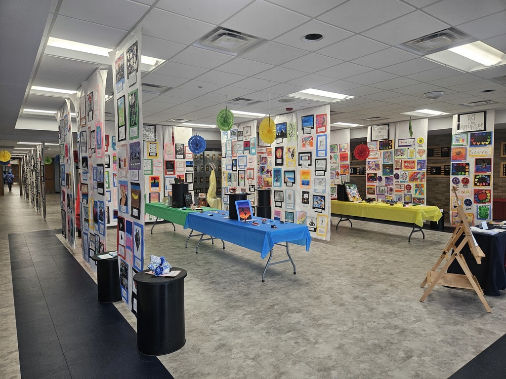 Middle School art projects displayed on white paper hanging from the ceiling and sitting on tables. 