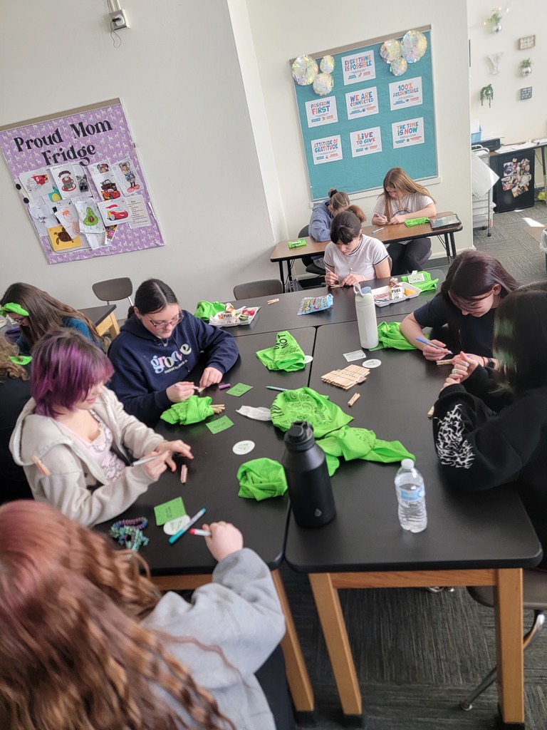 Students sitting at tables with markers and clothes pins with green shirts