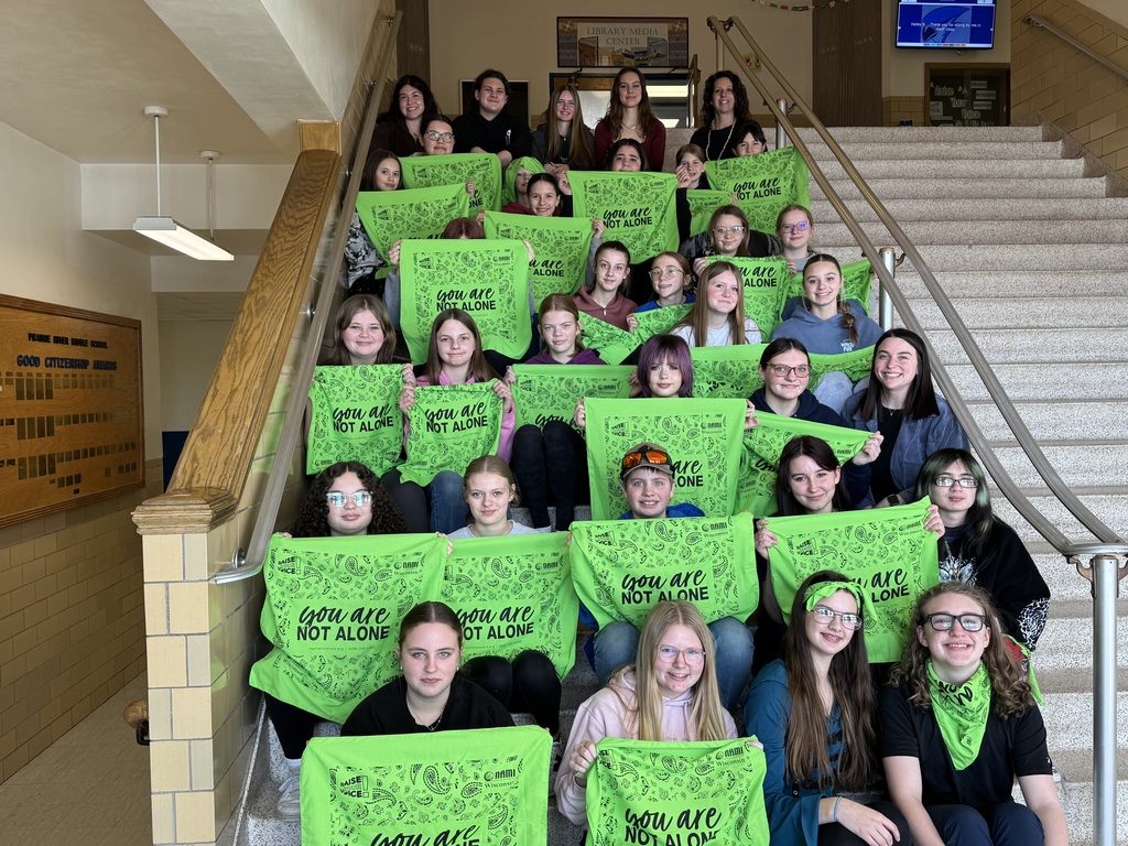 Students sitting on stairs at the middle school holding green shirts