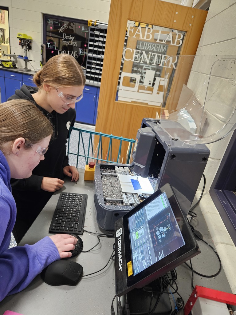 Two students at a computer looking at the 3D/Laser printer as it does a job
