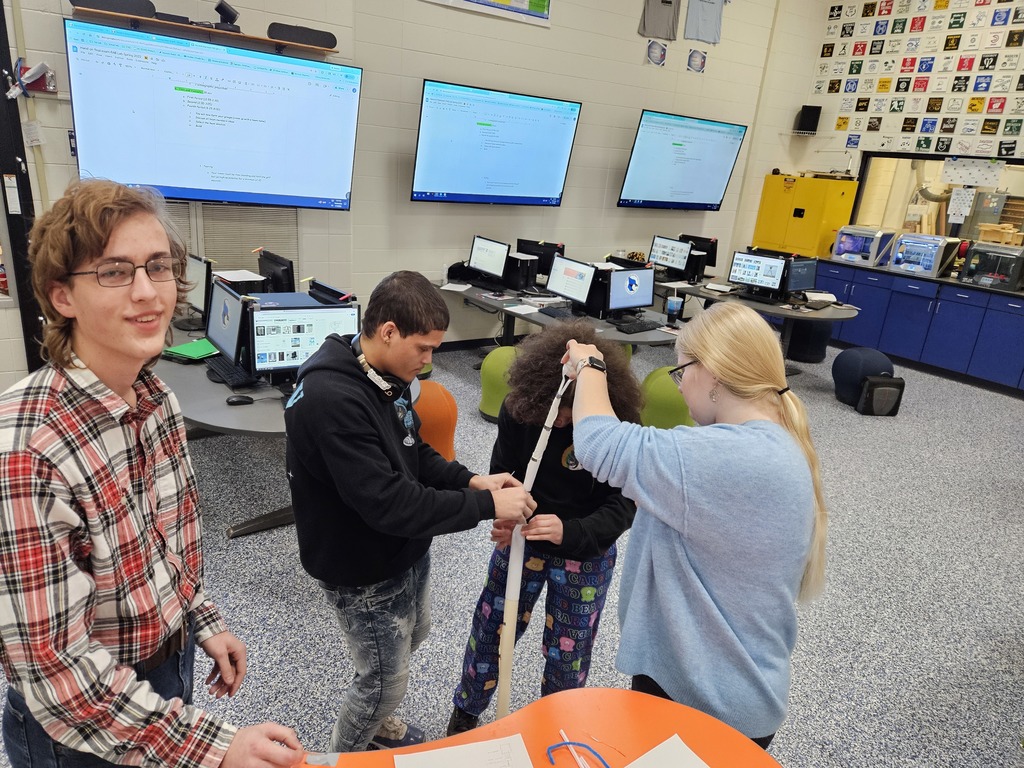 Three students measuring a rope while a student poses for the camera