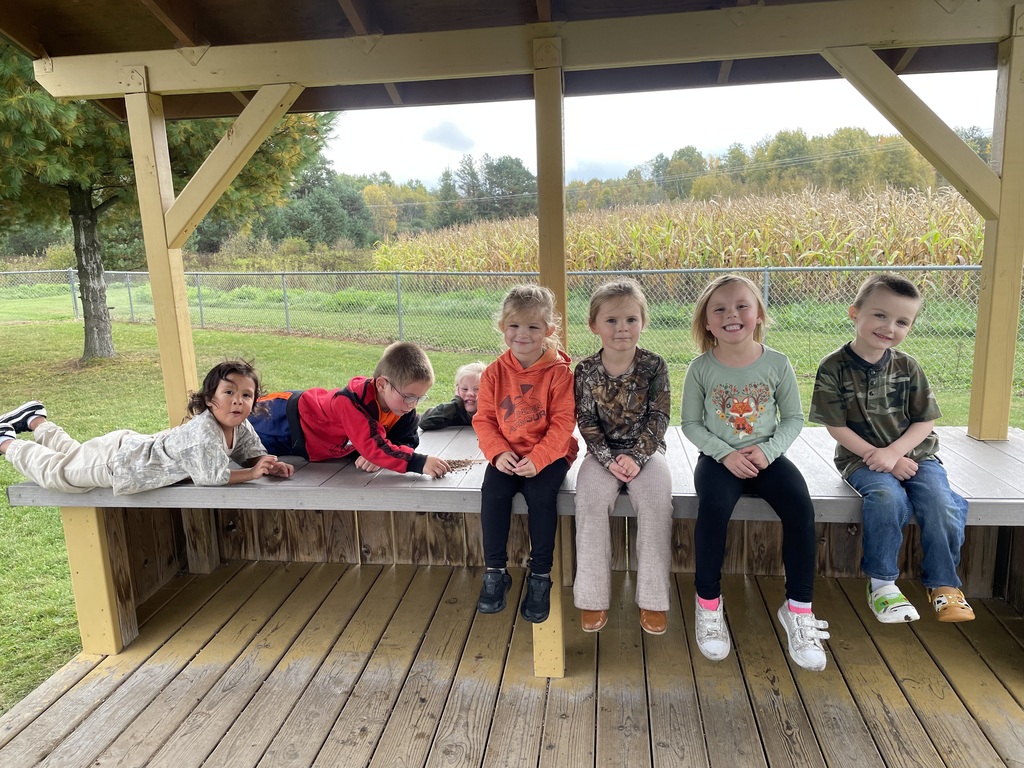 Students on a covered bench outdoors with a cornfield behind them