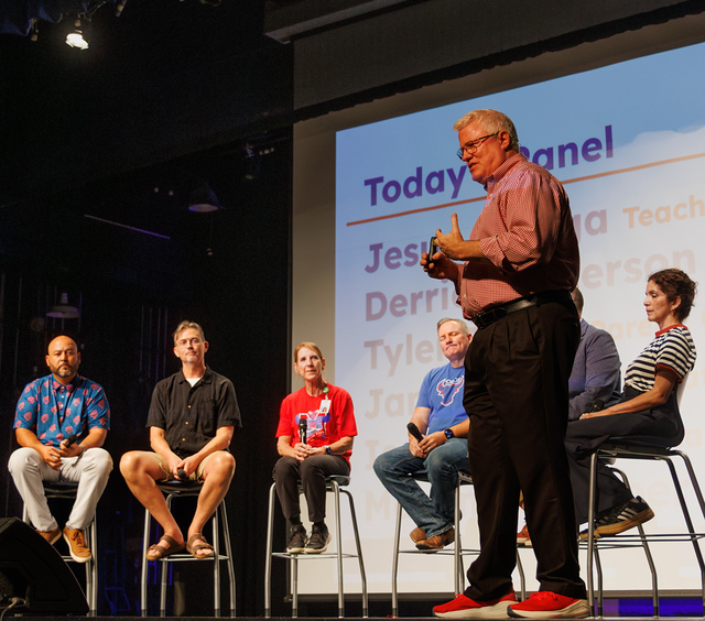 Principal Dr. Michael Oliver speaks on stage in an auditorium next to a panel of staff and community members seated on stools.