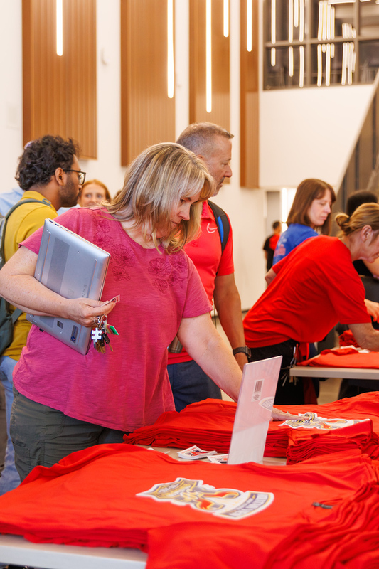 Woman holding a closed laptop looks at red Mountain View High School 50th anniversary t-shirts laid out on a table.