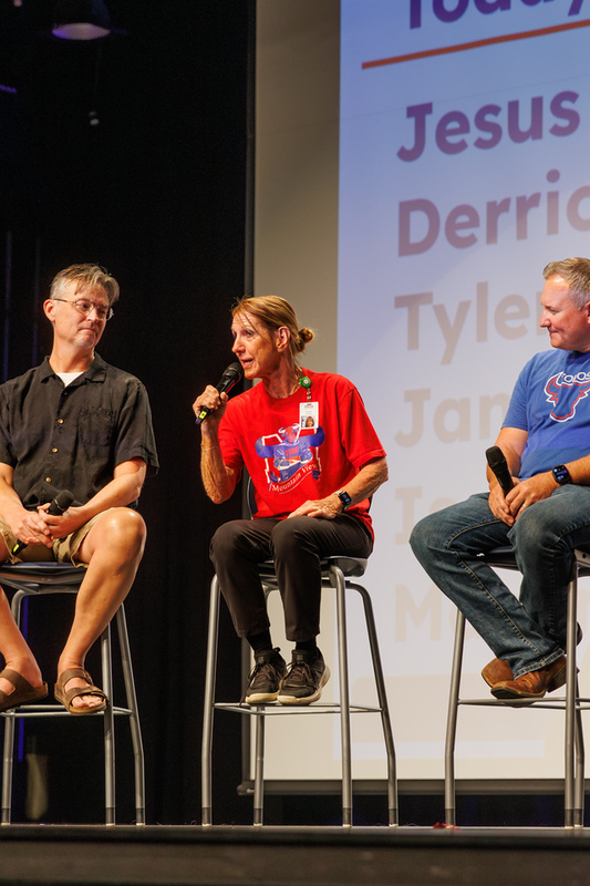 Staff member wearing a red Mountain View High School t-shirt speaks into a microphone while seated between other panel members.