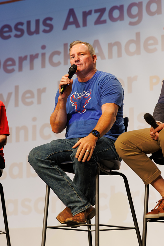 Panel member wearing a blue Mountain View Toros shirt speaks into a microphone while seated on stage.