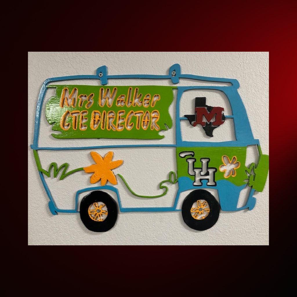 A colorful metal art piece with a bus design, labeled "Mrs. Walker CTE Director." The bus has green and blue stripes and yellow flowers.