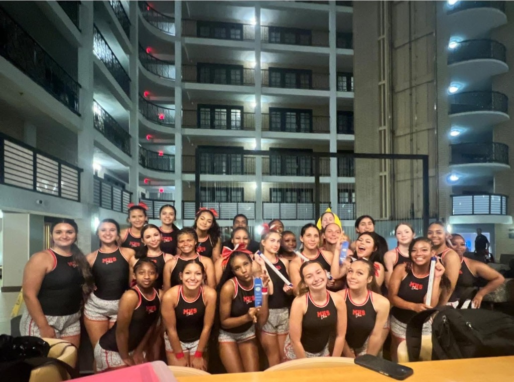 Group of young women in matching uniforms, standing in front of a multi-story building at night.
