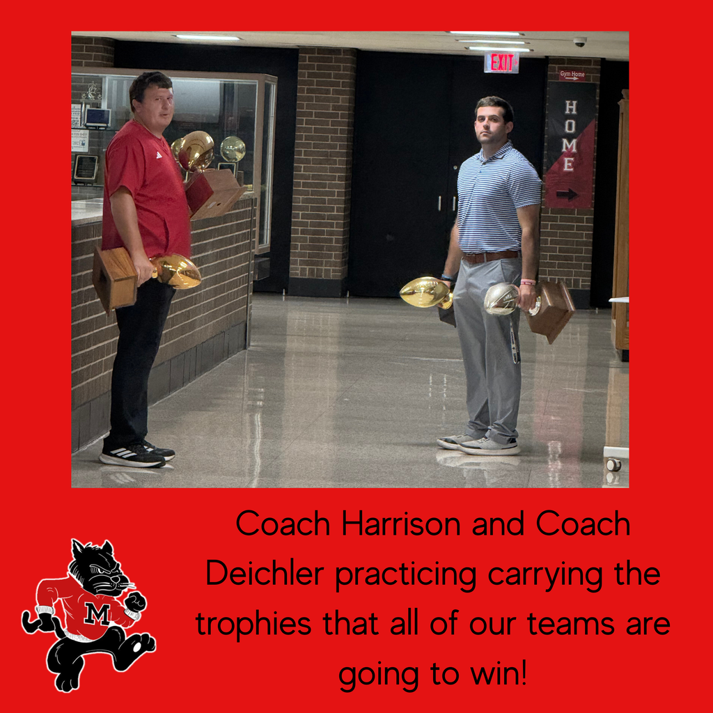 Two coaches stand in a hallway with trophies. One holds a golden trophy, and the other has a bronze one.
