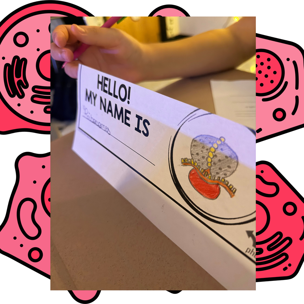 A desk displays a name tag with "Hello! My Name Is" and an illustrated diagram of a cell.