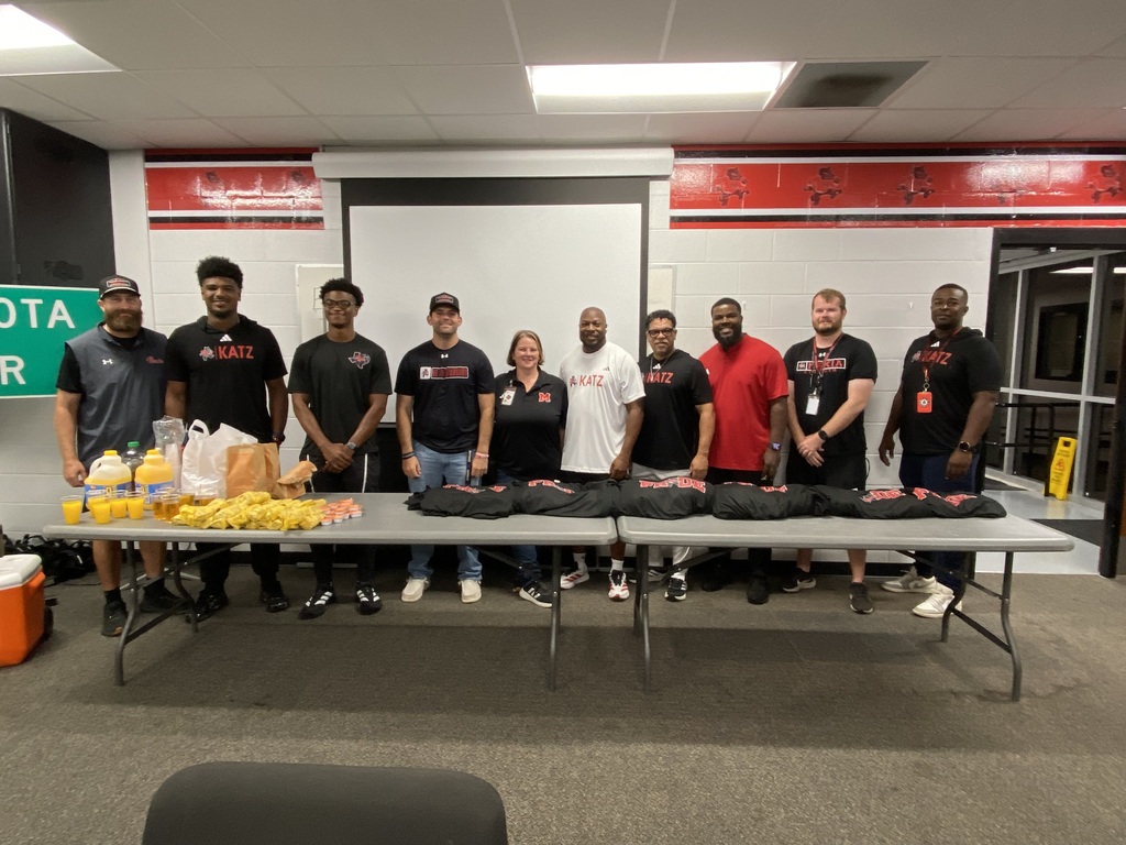 A group of people dressed in black shirts, standing behind a table with food items. A whiteboard is behind them.