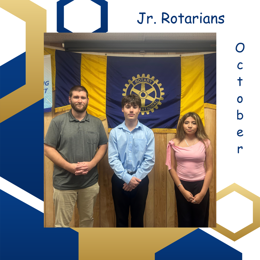 Three people stand in front of a wooden wall and a yellow-blue Rotary International flag.